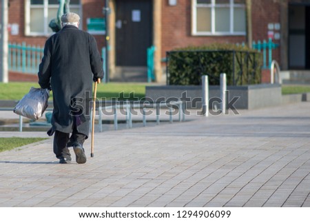 solitary old man walks alone with cane and shopping bag