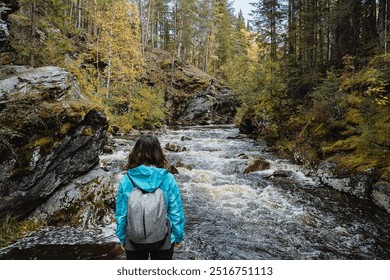 A solitary person stands by a flowing river, surrounded by autumn foliage and rocky terrain, embodying tranquility, peace, and a sense of exploration in nature - Powered by Shutterstock