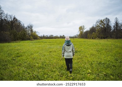 A solitary person strolls through a vast green field, surrounded by lush trees under a cloudy sky, appreciating the calming tranquility and natural beauty around - Powered by Shutterstock