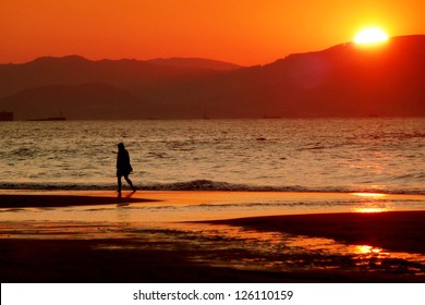 Solitary Person Walking In The Beach At Sunset