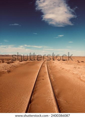 A solitary railway stretches across the vast desert, its iron tracks disappearing into the distant heat haze, symbolizing an arduous journey through the desolate landscape.