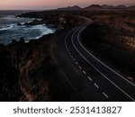 A solitary road winds along the rugged coastline during dusk, framed by dramatic cliffs and the ocean