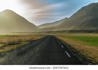 A solitary road winds through the majestic Icelandic mountains, illuminated by the warm hues of a stunning sunset. This serene scene captures the tranquil beauty  - Powered by Shutterstock