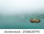 A solitary rock emerges from the Lake Haiyaha and mist above a serene turquoise lake in early morning light