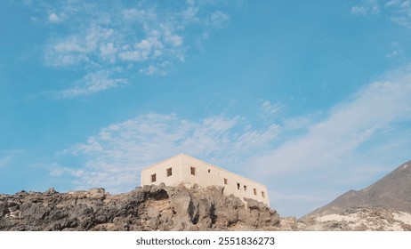 A solitary, rustic house stands on a rocky outcrop overlooking a vast expanse of sky - Powered by Shutterstock