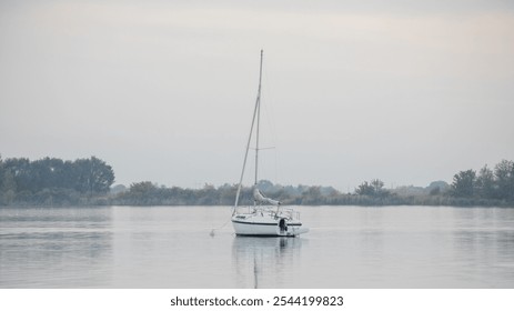 A solitary sailboat floats peacefully on a misty lake, perfect for concepts of tranquility and escape - Powered by Shutterstock