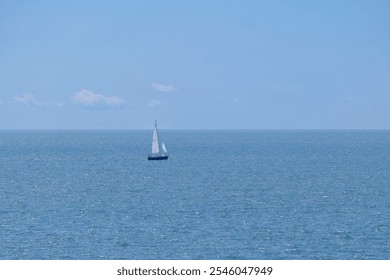 A solitary sailboat glides across the vast ocean under a clear blue sky. High quality photo - Powered by Shutterstock