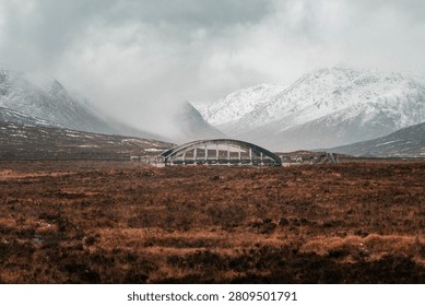 A solitary structure set against a dramatic snowy mountain backdrop under a cloudy sky in a remote landscape.