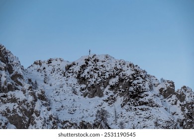 Solitary summit cross stands atop snow-covered mountain peak Mallestiger Mittagskogel, Karawanks, Carinthia, Austria. Rugged and rocky with patches of snow and exposed rock. Austrian Alps in winter - Powered by Shutterstock