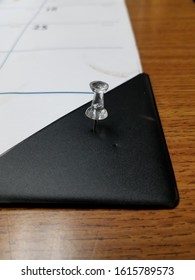 A Solitary  Thumb Tack On A Desk Calendar. 