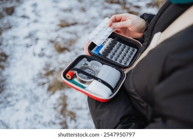 A solitary traveler in a stunning snowy setting holds an open first aid kit, highlighting the crucial importance of being prepared for emergencies during adventurous journeys - Powered by Shutterstock