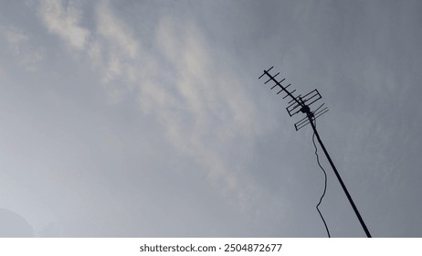 A solitary TV antenna silhouetted against a softly lit, cloudy sky during dawn. The minimalistic composition highlights themes of communication, technology, and simplicity in urban settings. - Powered by Shutterstock