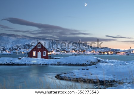 Solitary typical Norwegian red wooden Rorbu house in the snow at sunset