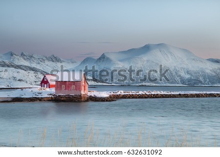 Solitary typical Norwegian red wooden Rorbu boat house in the snow at sunset