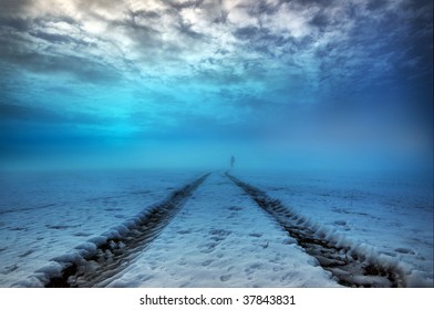 Solitary walker following tractor tire tracks into the mist through a snowy field - Powered by Shutterstock