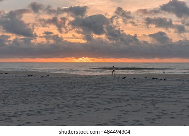 A solitary walker on the beach shortly after sunrise with footsteps etched in the sand leading to the ocean with breaking waves and fiery orange sunlight straining to burst through the clouds. - Powered by Shutterstock