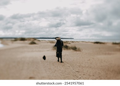 A solitary woman stands on a windswept beach, with her hair and scarf blowing in the breeze under a cloudy sky, evoking a sense of introspection and peaceful solitude in nature's vastness - Powered by Shutterstock