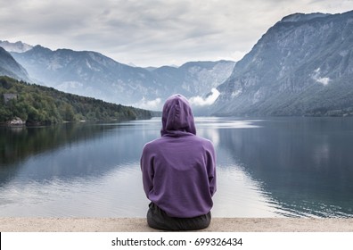 Solitary woman wearing purple hoodie watching tranquil overcast morning scene at lake Bohinj, Alps mountains, Slovenia. - Powered by Shutterstock