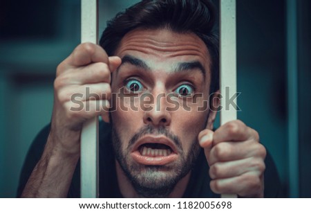 Solitude concept, man behind prison or cage bars trying to break free, mentally ill and deranged