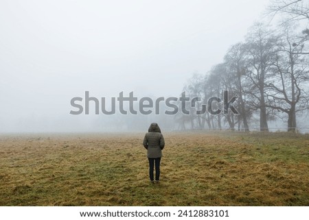 Solitude female person in the fog. Lonely woman in hooded coat standing in foggy nature. Loneliness concept