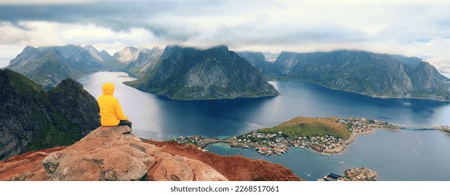 Solitude with nature. Panoramic aerial view of fjord and fishing village. Man tourist sitting on a cliff of rock. Beautiful mountain landscape. Nature Norway, Lofoten islands.  #UniqueSSelf - Powered by Shutterstock