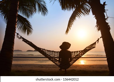 solitude, silhouette of woman in hat sitting alone  in hammock at sunset on the beach
