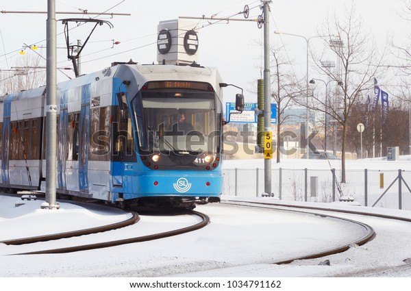 Solna, Sweden - February 27, 2018: Stockholm\
transport suburban rapid transit tramway with a blue tram class A32\
on the Tvarbanan system in service for SL on line 22 enters Solna\
Business park.