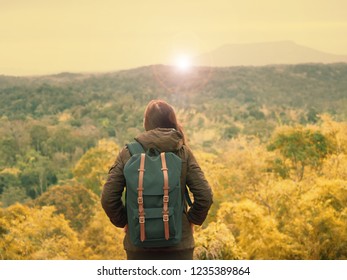 solo backpack and camping concept from backside of long hair woman in warm cloth with her bag travel, relax, happy  and see to forest and mountain in morning after sunrise