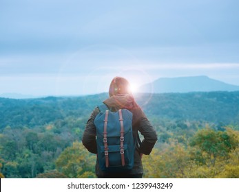 solo backpack and camping concept from backside of long hair woman in warm cloth with her bag travel, relax, happy  and see to forest and mountain in morning after sunrise