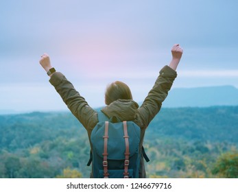 solo backpack and camping concept from backside of long hair woman in warm cloth with her bag travel, relax, happy  and show her hand and see to forest and mountain in morning after sunrise