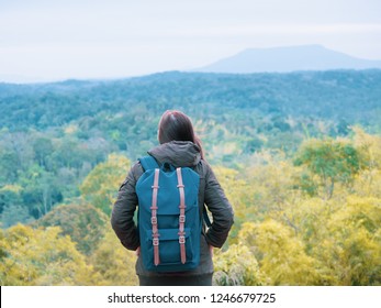solo backpack and camping concept from backside of long hair woman in warm cloth with her bag travel, relax, happy  and see to forest and mountain in morning after sunrise