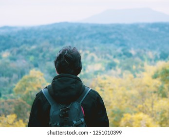 solo backpack and camping concept from backside of black hair man in warm hoodie sweatshirt with his bag solo travel, relax, happy  and see to forest and mountain in morning after sunrise