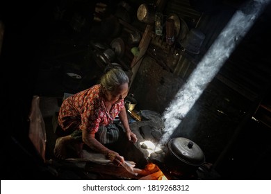 Solo, Central Java Indonesia On November 17th, 2018: Asian Old Woman Cooking At Her Traditional Javanese Kitchen, Using Dry Wood For Its Fire Source, Under Exposure On Dark Place To Make Ray Of Light 