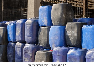 Solo, Central Java, Indonesia - September 19, 2025: Black and blue plastic barrels are stacked in a warehouse under a clear blue sky. The scene conveys a sense of industrial organization and efficienc