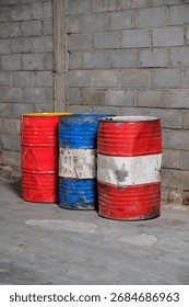 Solo, Central Java, Indonesia - September 30, 2025: Three Rusty Oil Barrels on Concrete Wall in Industrial Yard