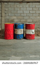 Solo, Central Java, Indonesia - September 30, 2025: Three Rusty Oil Barrels on Concrete Wall in Industrial Yard