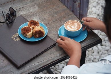 Solo, Central Java, Indonesia-2021, Selective Focus Of Coffee Latte In A Blue Cup On The Table Took By The Hand 