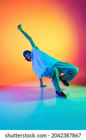 Solo Dance Performance. Portrait Of Young Man, Hip-hop Dancer In Stylish Clothes In Action Isolated On Colorful Background At Dance Hall In Neon Light. Youth Culture, Movement, Fashion, Action.