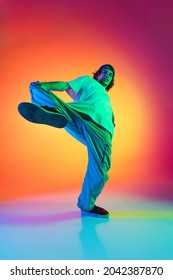 Solo Dance Performance. Portrait Of Young Man, Hip-hop Dancer In Stylish Clothes In Action Isolated On Colorful Background At Dance Hall In Neon Light. Youth Culture, Movement, Fashion, Action.