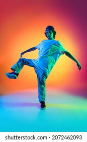 Solo Dance Performance. Portrait Of Young Man, Hip-hop Dancer In Stylish Clothes In Action Isolated On Colorful Background At Dance Hall In Neon Light. Youth Culture, Movement, Fashion, Action.