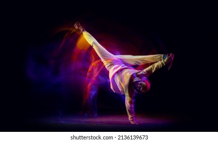 Solo dance. Young flexible sportive man dancing hip-hop in white outfit on dark background in mixed yellow neon light. Beauty, sport, youth, action, moves. Dancer shows breakdance figures