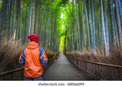 Solo Male Traveler Standing From Behind At The Green Bamboo Forest In Arashiyama, Kyoto, Japan, Wearing Winter Orange And Red Clothes Looking At The Long Path.