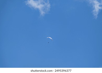 Solo paraglider flying high in a clear blue sky dotted with white clouds, epitomizing freedom and excitement - Powered by Shutterstock