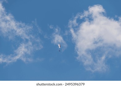 Solo paraglider flying high in a clear blue sky dotted with white clouds, epitomizing freedom and excitement - Powered by Shutterstock