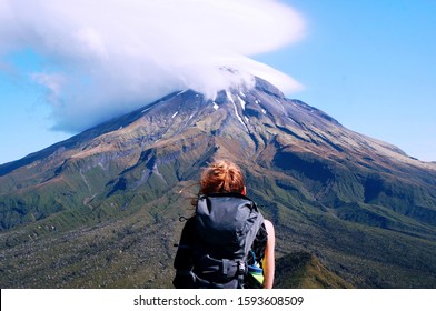 Solo traveler with backpack looking on the most iconic mountain in North Island, New Zealand. Top of Taranaki is hidden in the cloud. On top is still some snow, but on the bottom is a fresh green line - Shutterstock ID 1593608509