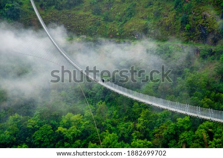 A solo walk in the midst of nature , a person crosses the suspension bridge connecting Baglung and Parbat districts of Nepal . Image taken in 2020