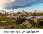 Solovetsky Monastery on the Solovetsky Islands, the blue water of the Bay of Prosperity in the rays of the setting autumn sun and old wooden boats on the shore