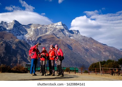 SOLUKHUMBU, NEPAL - NOVEMBER 19 ,2019 : Four Hikers In Red Winter Jacket Are Doing Group Selfie In Everest Base Camp Trek With Blue Sky And Himalayan Mountain Range At The Background.