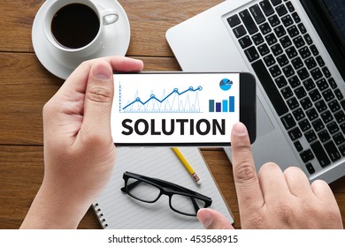 SOLUTION ( Solution Innovation Progress Strategy Decision ) message on hand holding to touch a phone, top view, table computer coffee and book
