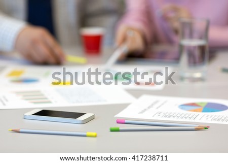 Solving Business Issue Concept - grey Office Table with Color professional Charts on Papers Pencils and Electronic Gadgets blurred Body of Businesspeople on Background